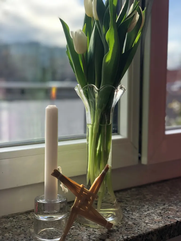 Brigid-Kreuz aus Stroh mit weißer Kerze und Tulpen am Fenster